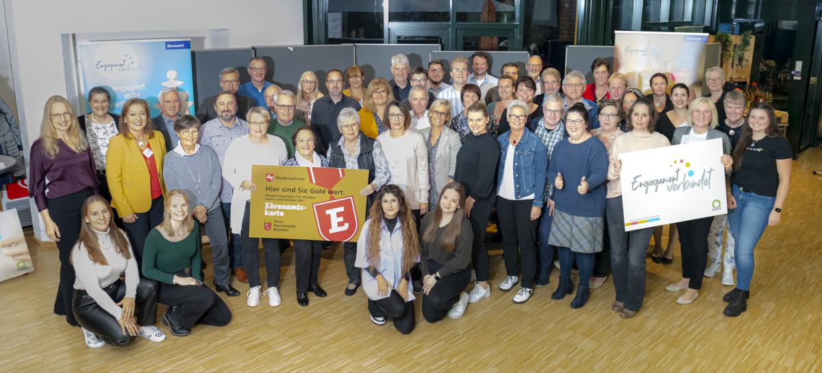 Eine große Personengruppe hat sich im Halbkreis aufgestellt und schaut in die Kamera.