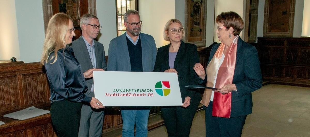 Zukunftsregion Fünf Personen stehen in einem historischen Raum und halten ein Schild .