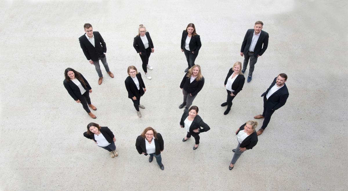 Teambild-Transferagentur Eine Personengruppe steht auf einem hellen Fußboden und schaut nach oben.
