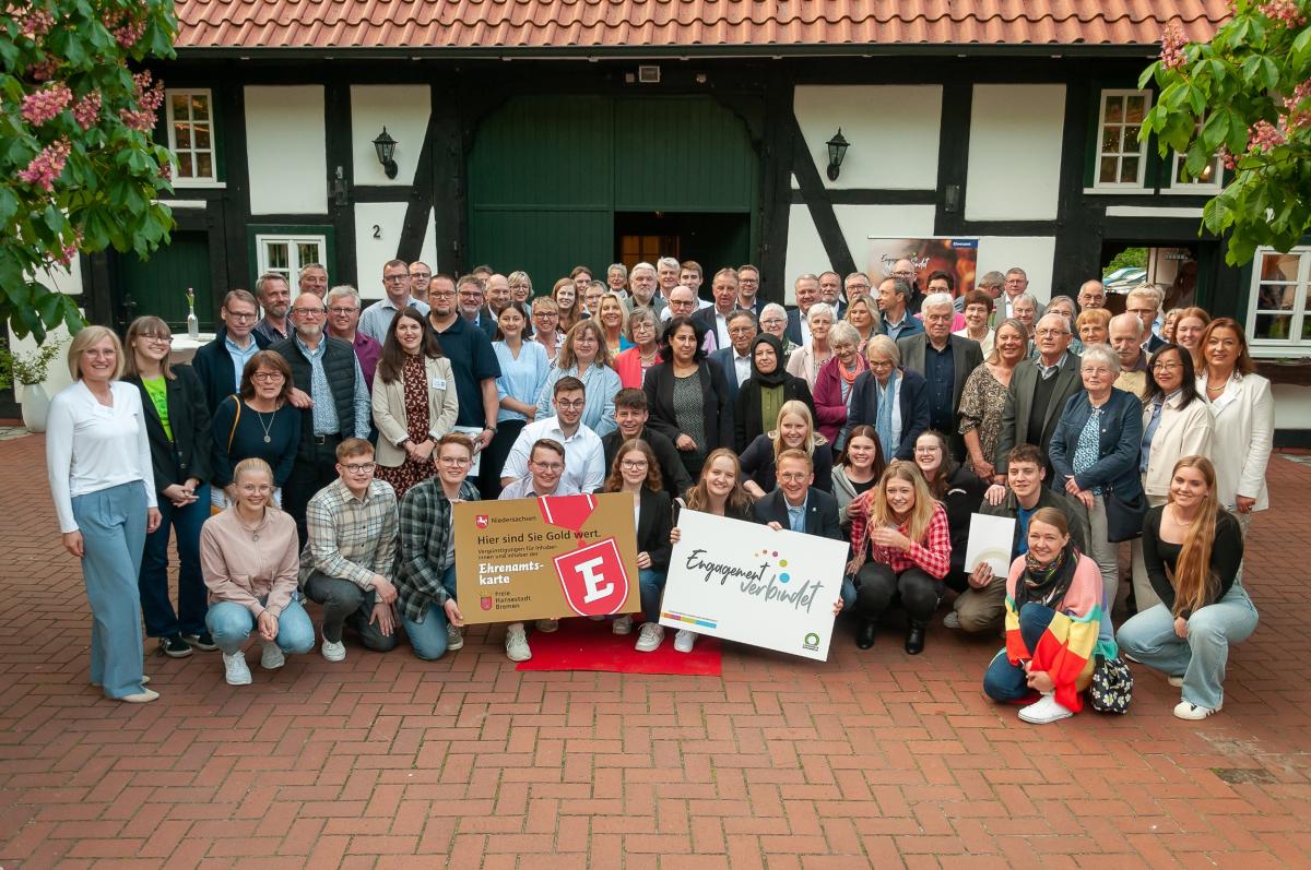 Eine große Personengruppe steht und hockt vor einem Fachwerkhaus.