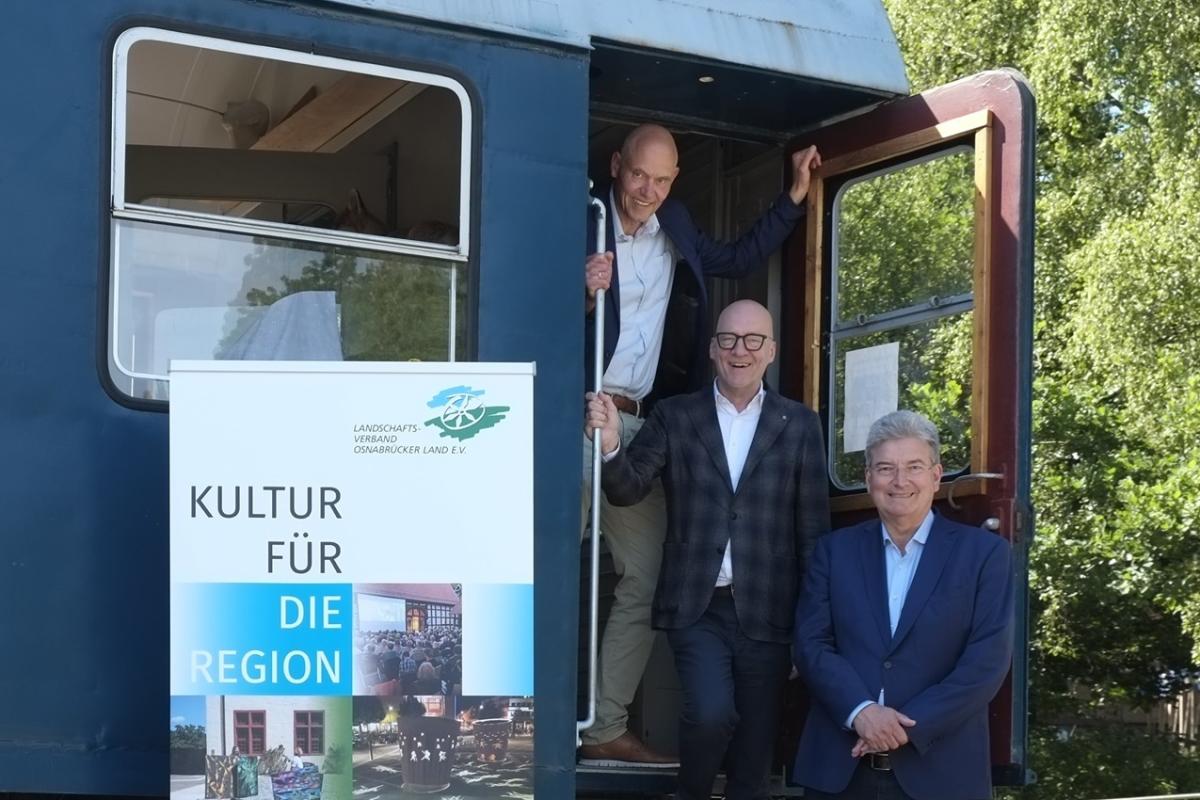 Drei Personen stehen am Einstieg eines Eisenbahnwaggons.
