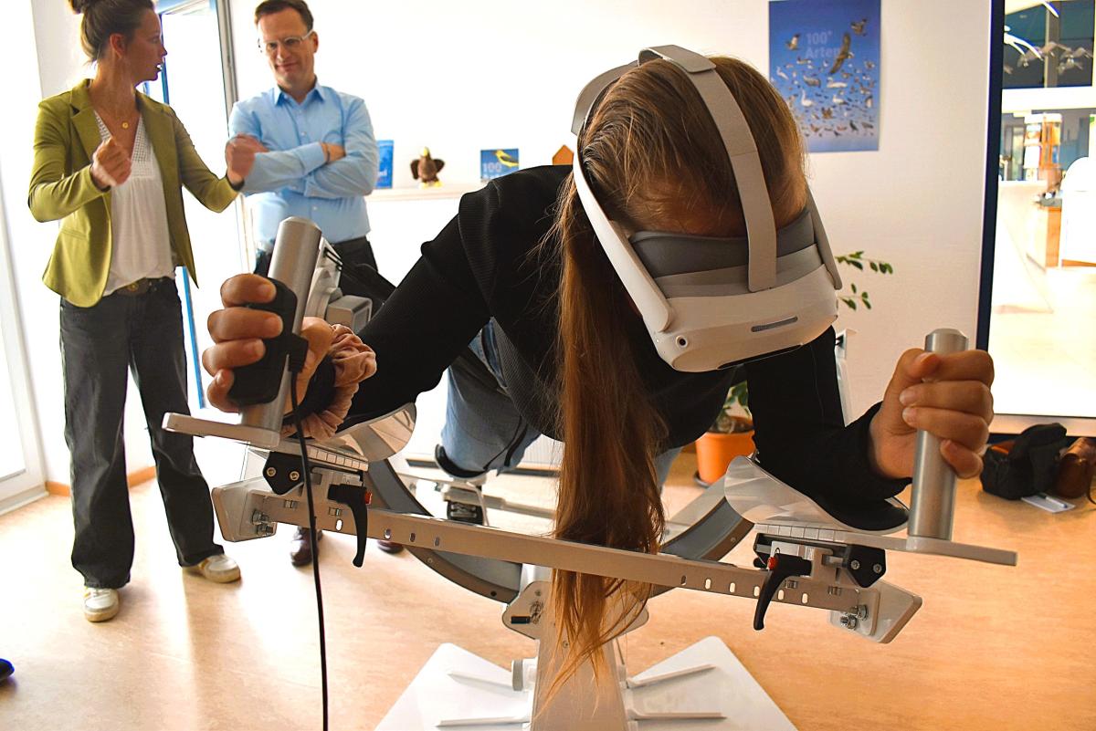 Eine Person mit VR-Brille liegt auf einem Flugsimulator