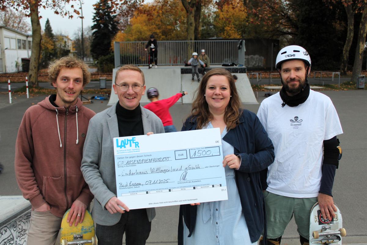 Vier Personen auf einem Skateplatz mit einem symbolischen Scheck.