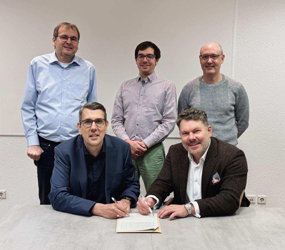 Fünf Personen stehen und sitzen hinter einem Tisch.