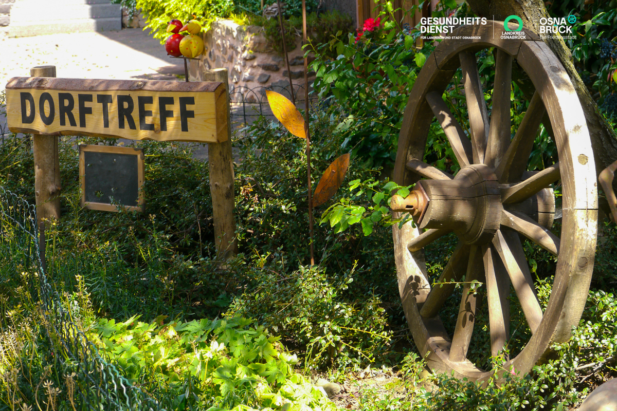 Wagenrad und Holschild mit der Aufschrift Dorftreff in einem Garten