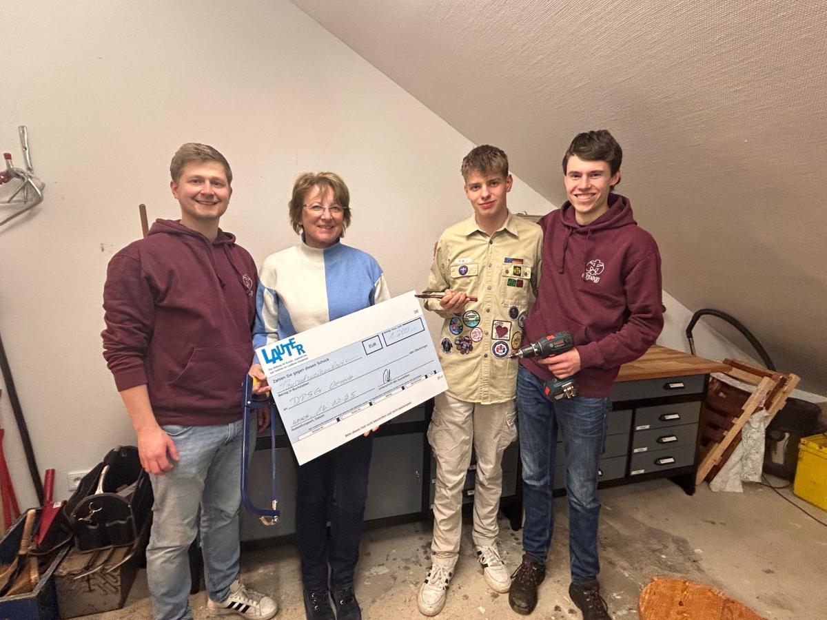 Vier Personen mit Spendenscheck stehen in einem Raum mit Dachschräge.