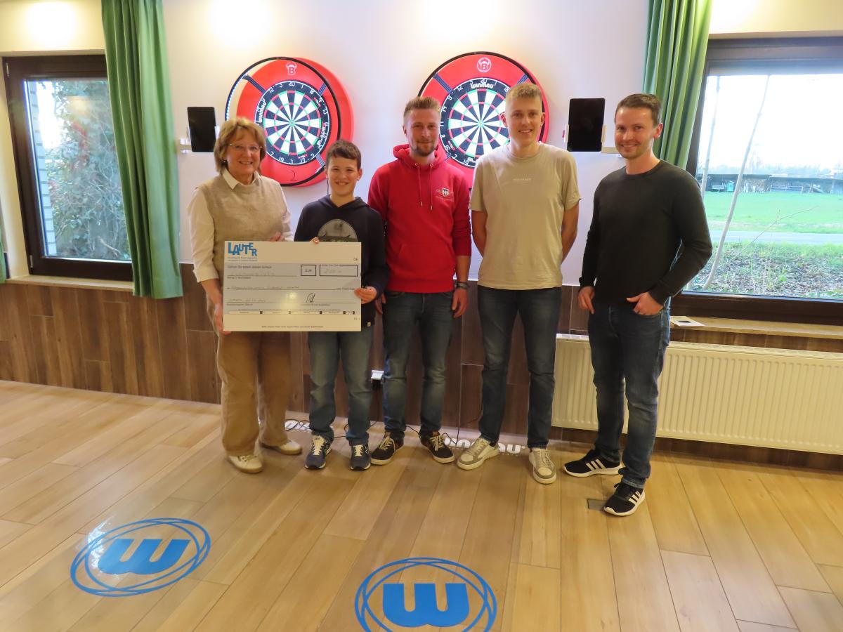 Fünf Personen mit einem symbolischen Scheck stehen vor zwei Dartscheiben