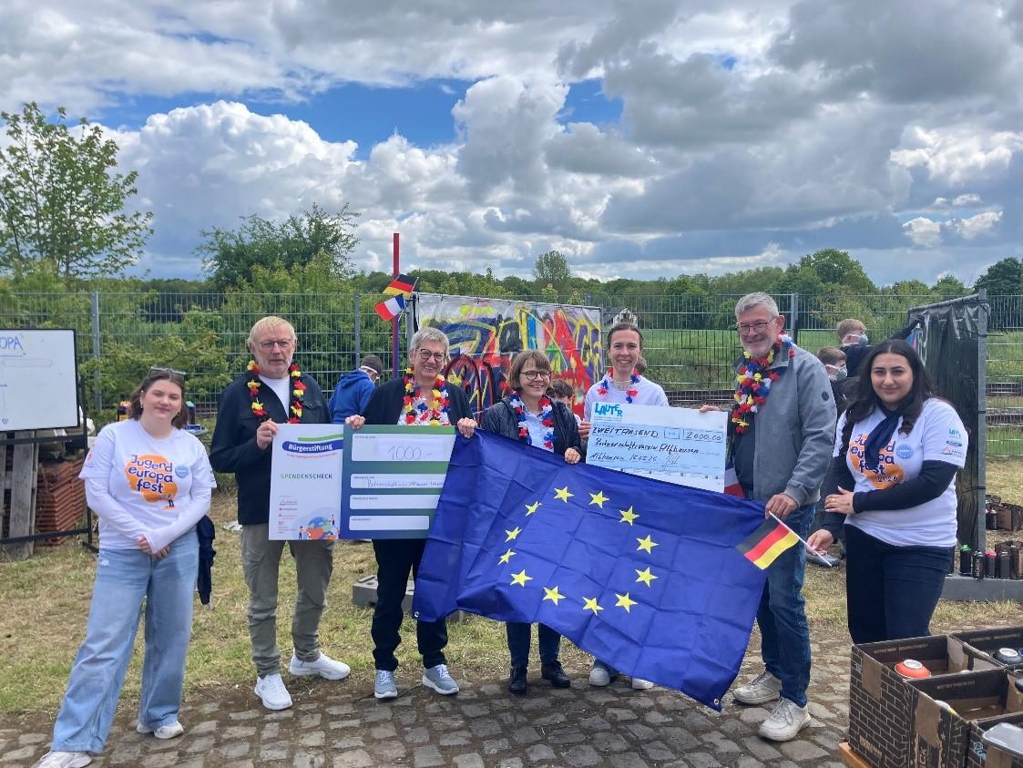 Sieben Personen mit Europa- und Deutschlandflagge stehen auf einem Platz unter freiem Himmel