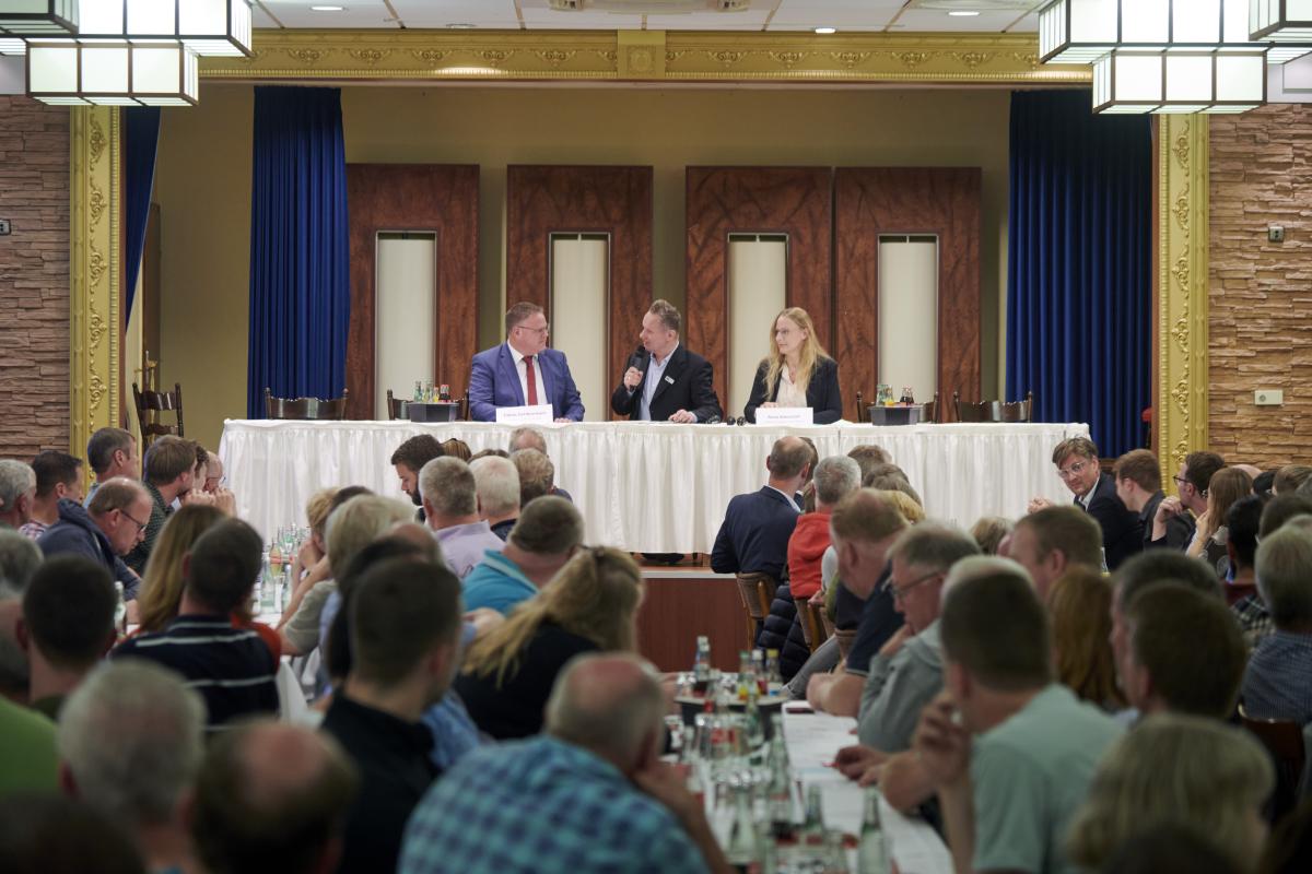 Drei Personen sitzen auf einer Bühne vor sich Publikum