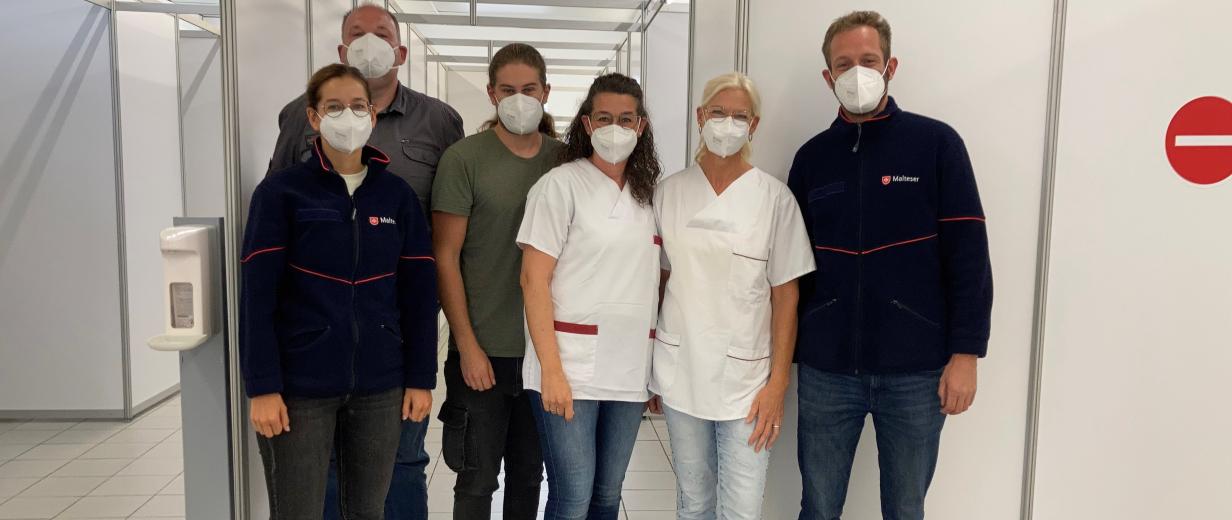 Sechs Personen mit Gesichtsmasken stehen in einem Impfzentrum