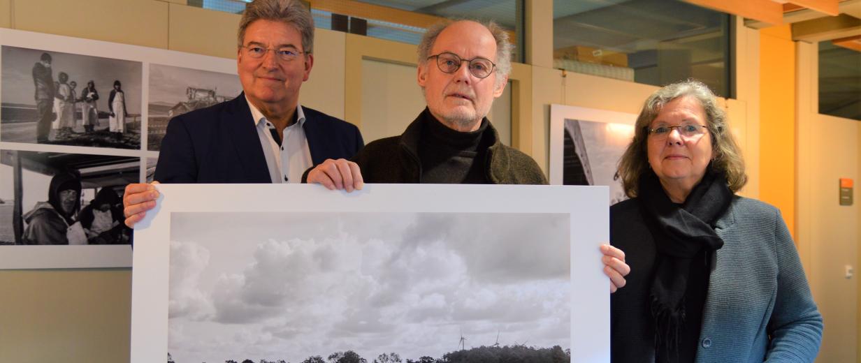 Drei Personen stehen in einem Flur und halten ein großformatiges Schwarz-weiß-Foto in den Händen.