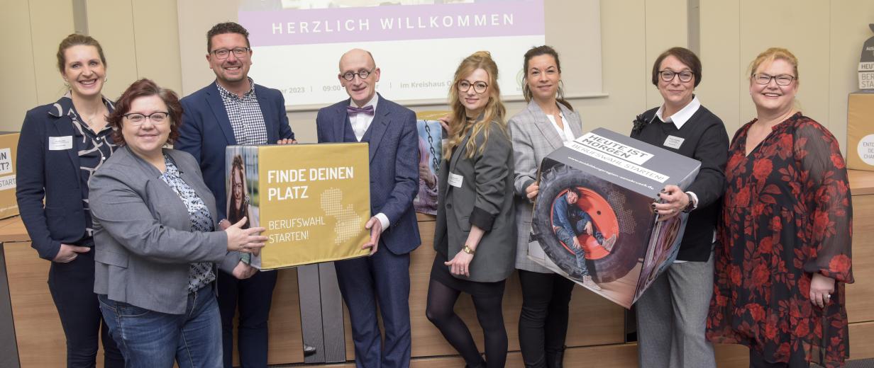 Fachtagung vom Stift zum Schreiber Eine Personengruppe mit bedruckten Schaumstoffwürfeln in den Händen steht vor einer Video-Projektionsfläche.