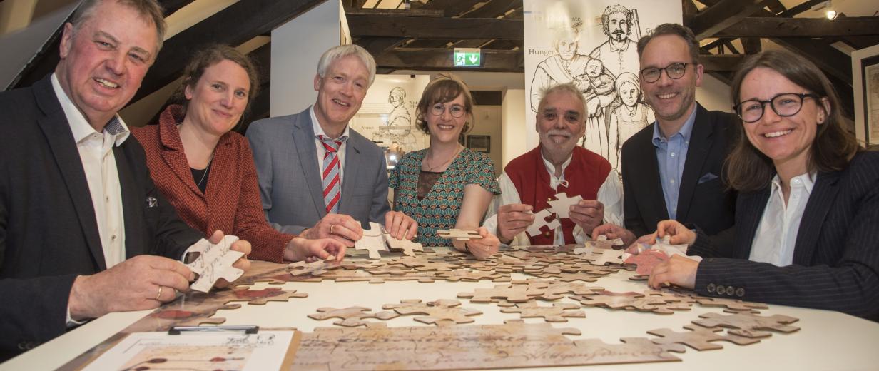 Ausstellung Lebensbilder Museum im Kloster Sieben Personen stehen um einen Tisch herum, auf dem ein Puzzle liegt.
