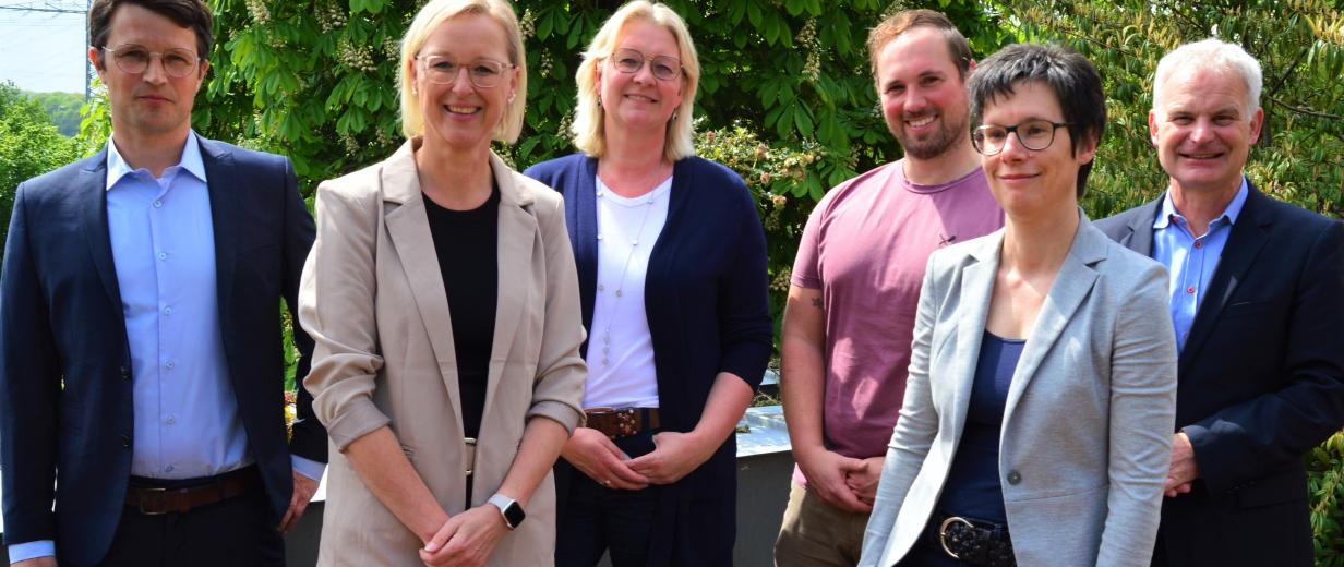 Sechs Personen stehen auf einer Terrasse und schauen in die Kamera.