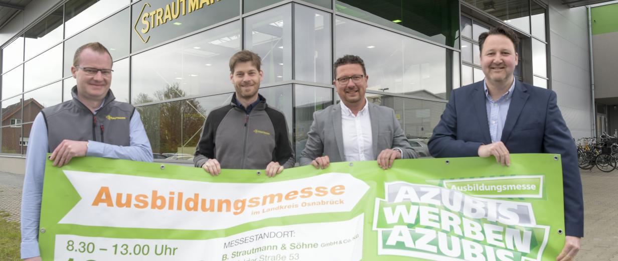 Azubis werben Azubis Strautmann Vier Personen stehen vor einem Firmengebäude mit Glasfassade und halten ein Banner in den Händen.