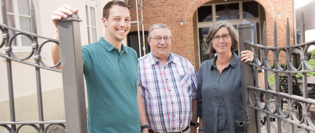 3 Personen vor Eingangspforte eines Hauses