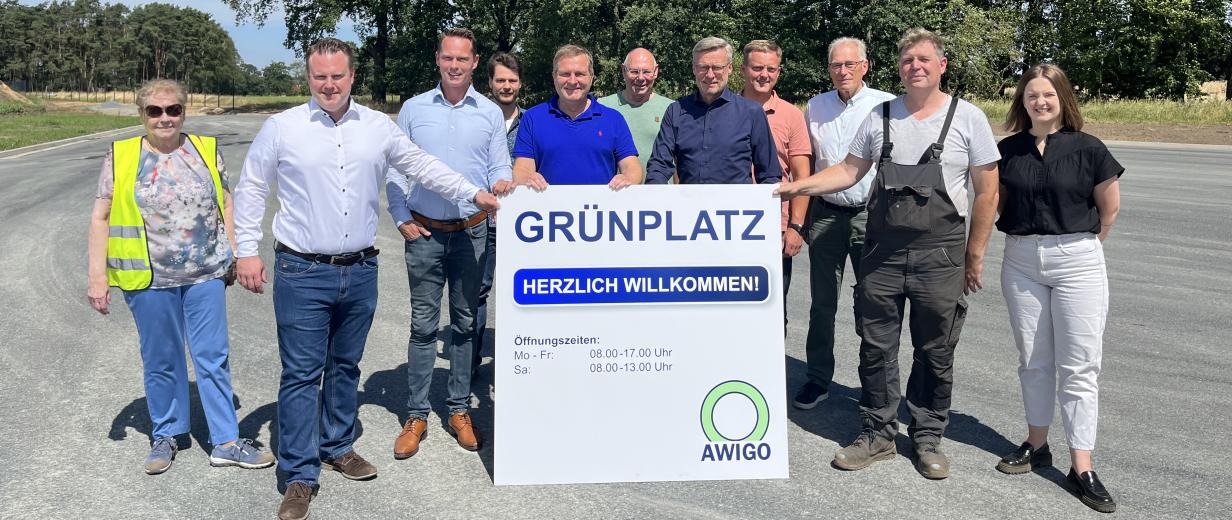 AWIGO Grünplatz Hollage Schwarzer See Eine Personengruppe steht auf einem großen Platz und hält ein Schild in den Händen.