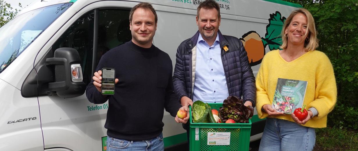 Drei Personen stehen vor einem Lieferwagen und halten Lebensmittel in die Kamera.