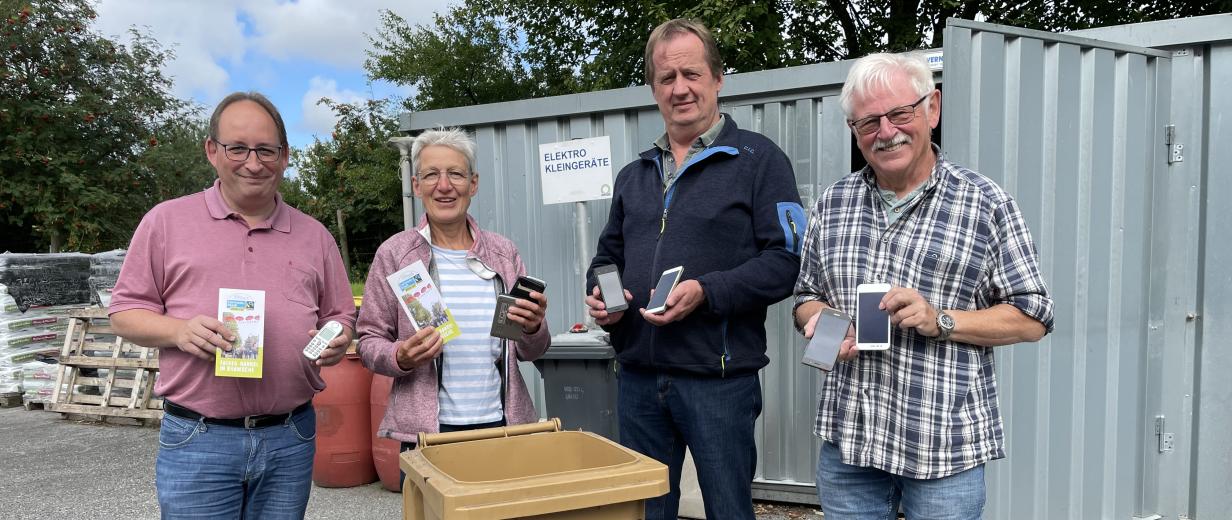 Althandy Recycling AWIGO Vier Personen stehen hinter einer Abfalltonne