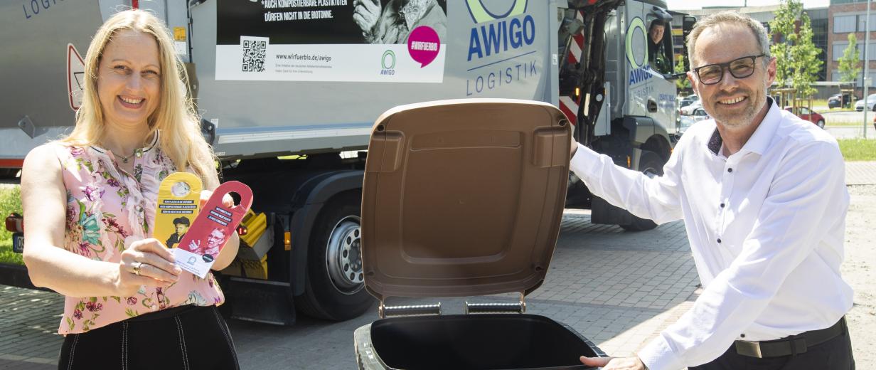 Zwei Personen stehen mit einer braunen Abfalltonne vor einem Müllauto.