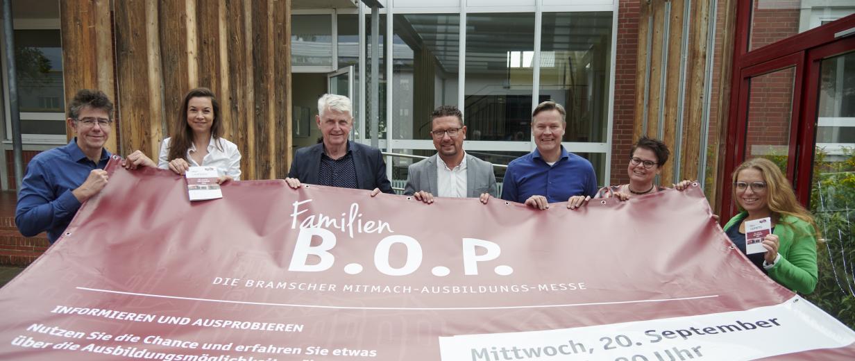 Sieben Personen mit einem Werbebanner in den Händen stehen vor einem Gebäude.