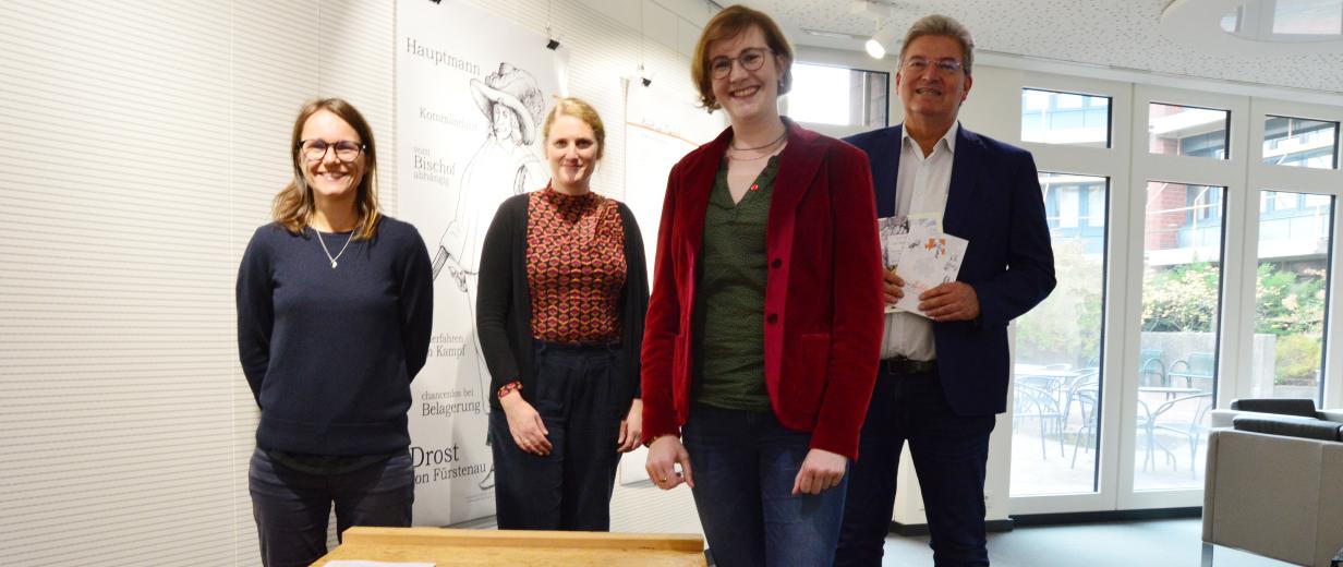 Vier Personen stehen in einem Foyer hinter einem Ausstellungsexponat.