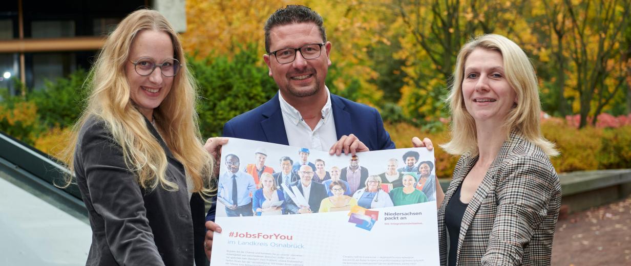 Jobmesse für Zugewanderte Drei Personen präsentieren ein Plakat.