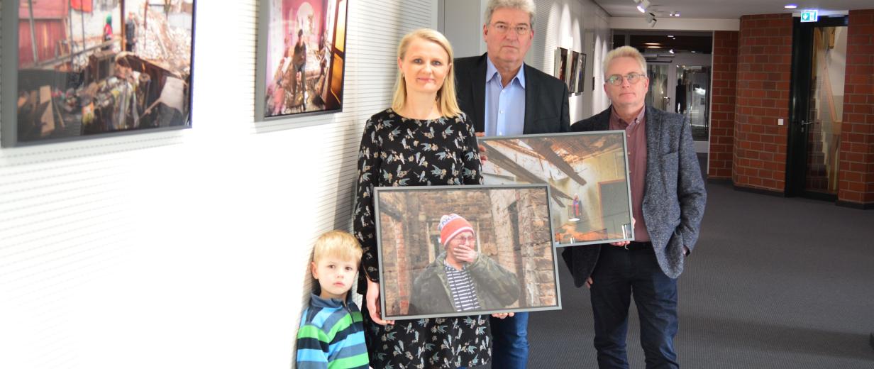 Vier Personen mit Fotos in den Händen stehen in einem Flur mit Fotos an den Wänden.