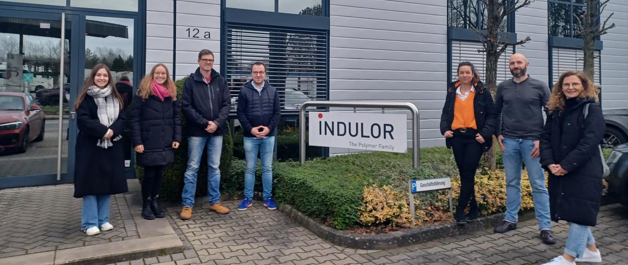 Indulor Bramsche MaßArbeit Eine Personengruppe steht vor dem Eingang zu einem Firmengebäude.