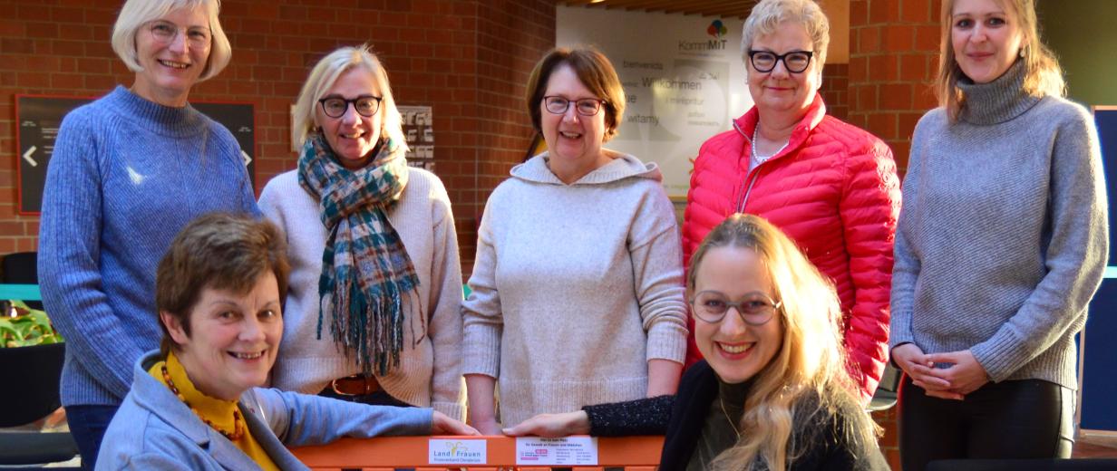 Orangene Bank LandFrauen Sieben Personen sitzen auf und stehen hinter einer orangenen Bank.