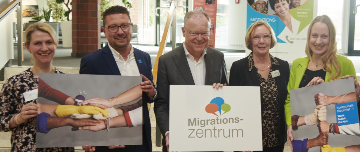 Fünf Personen stehen im Foyer eines Gebäudes vor einer Treppe.