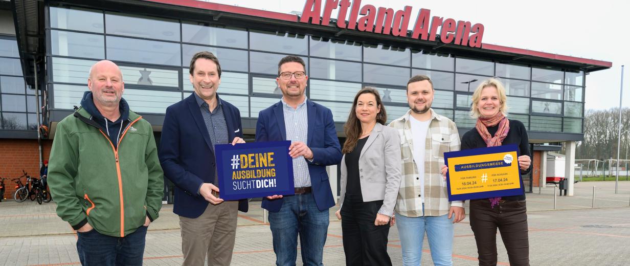 Sechs Personen stehen vor einer Halle mit Glasfassade.