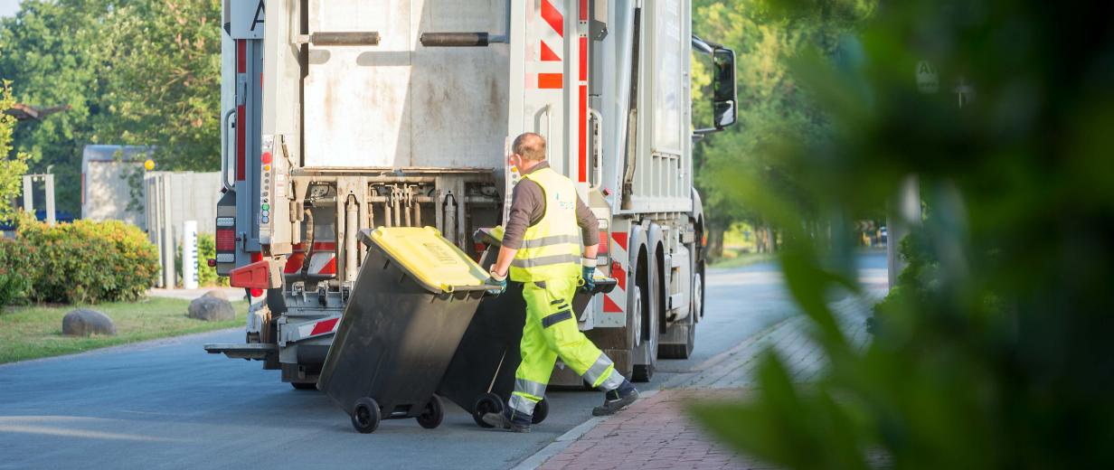 Eine Person rollt eine gelbe Tonne zu einem Abfallfahrzeug.