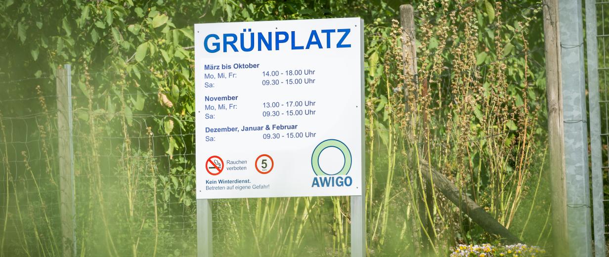 AWIGO Grünplätze Schild an einem Zaun mit Grünzeug dahinter
