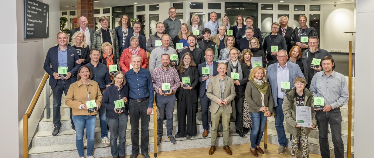 Verleihung Grüne Hausnummer 2024 Eine Personengruppe steht auf einer Treppe in einem Foyer.
