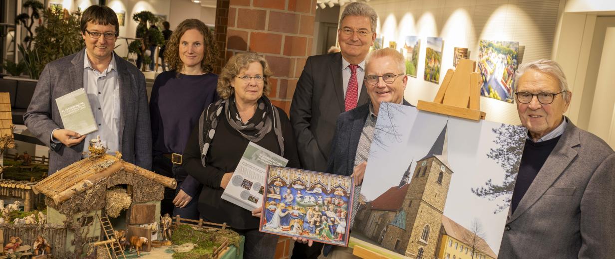 Krippenausstellung im Kreishaus Sechs Personen stehen neben einer Staffelei mit dem Foto einer Kirche.