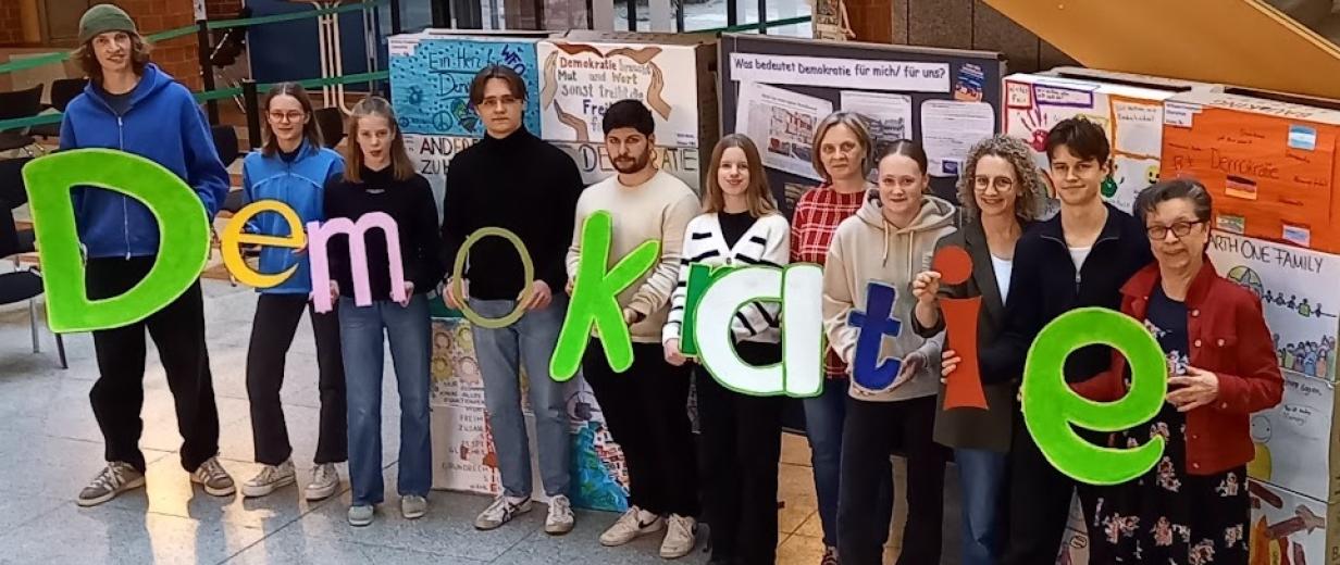 Meller Brandmauer, Ausstellung, Kreishaus Eine Personengruppe steht in einem Foyer und hält Buchstaben in den Händen, die das Wort Demokratie bilden.