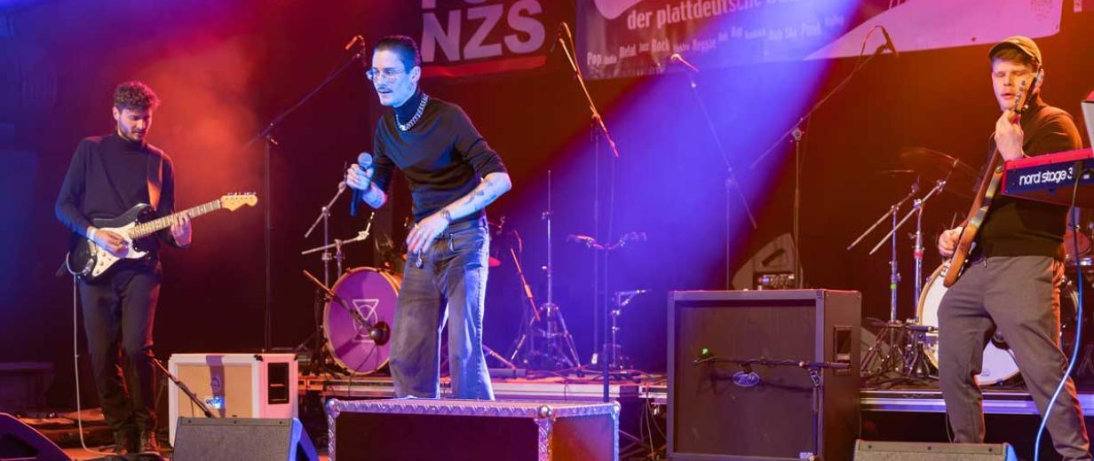 Plattsounds Finale 2024, Frry Drei Rockmusiker stehen auf einer Bühne.