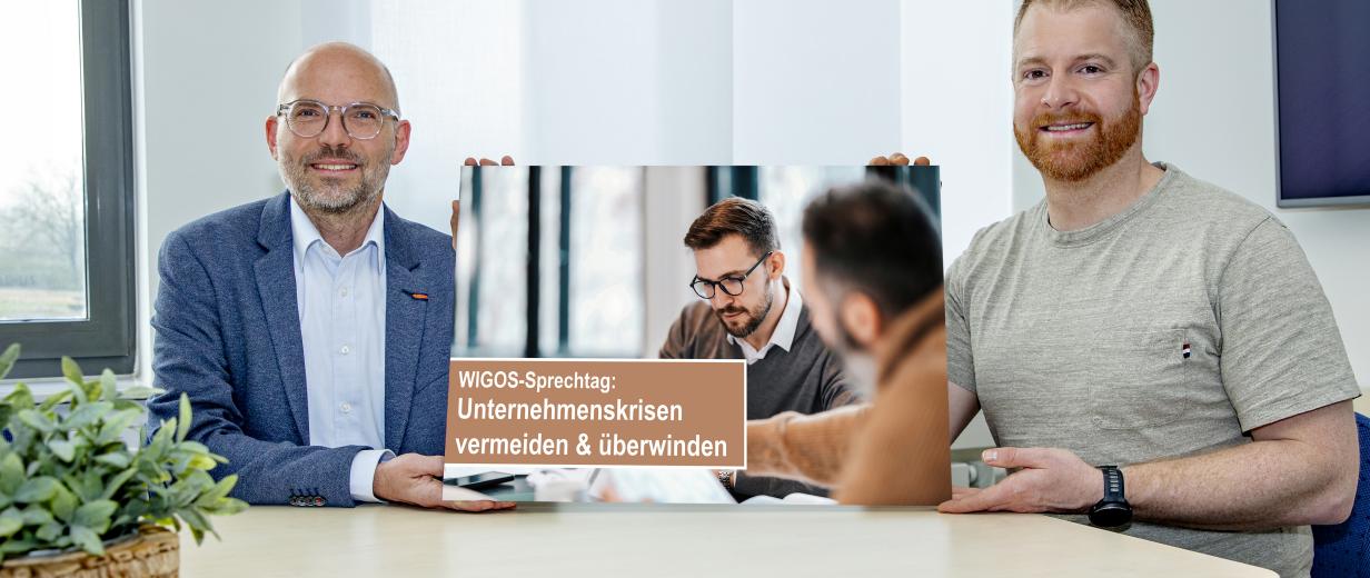 Zwei Personen sitzen an einem Tisch und halten eine Grafik in die Kamera.