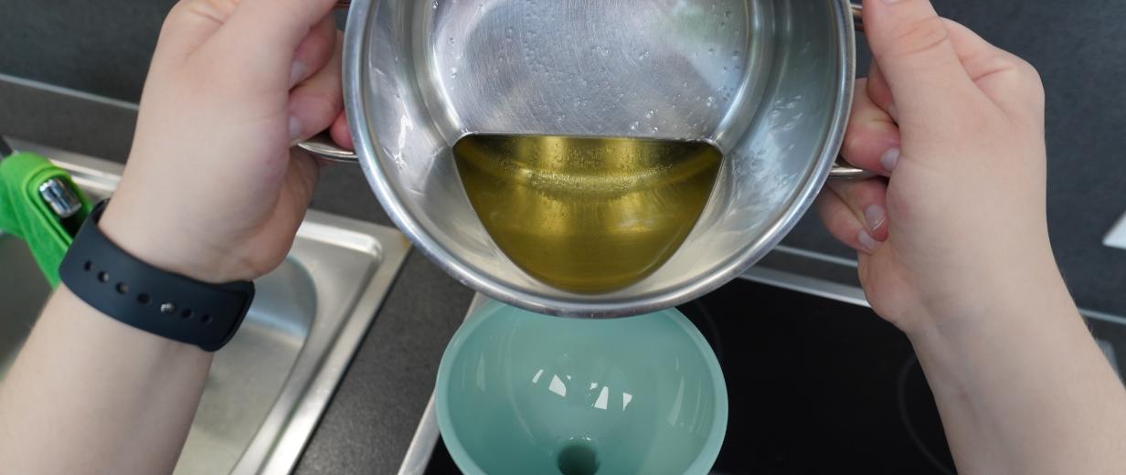 Öl wird aus einem Topf in eine Flasche mit Trichter gegossen.