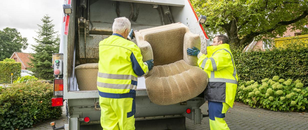 Zwei Personen entsorgen einen Sessel in einem Müllfahrzeug.