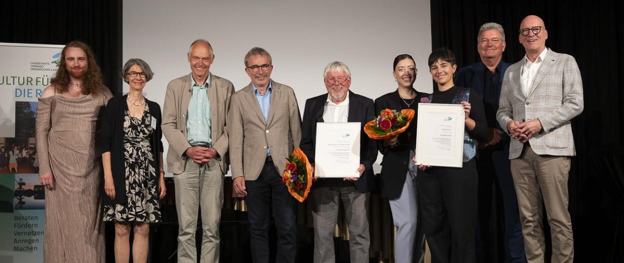 Eine Personengruppe steht auf einer Bühne.