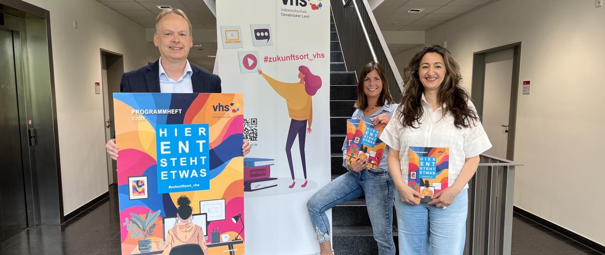 Semesterstart vhs Osnabrücker Land Drei Personen und ein Roll-Up-Poster stehen in einem Flur.