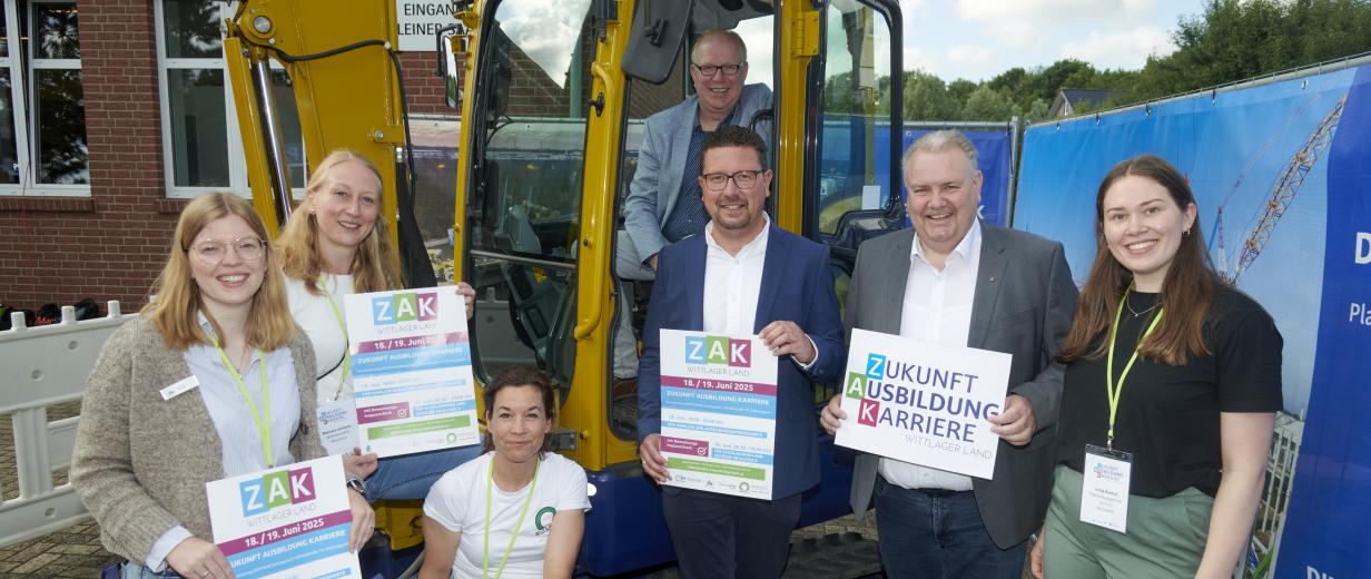 Sieben Personen stehen vor einem Bagger.