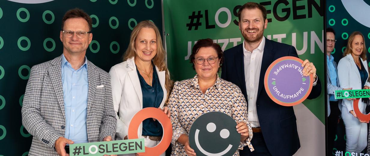 Vier Personen stehen vor einer Fotowand.