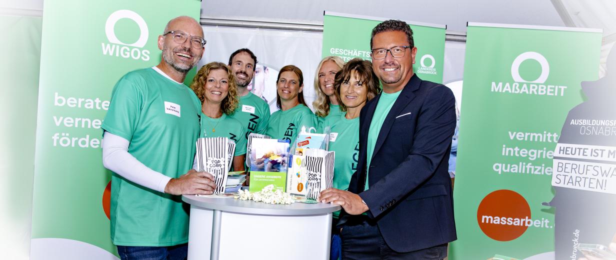 WIGOS und MaßArbeit beim Tag der Niedersachsen Eine Personengruppe steht an einem Messestand