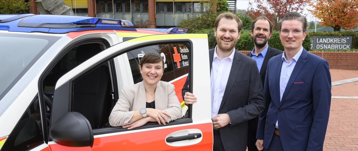 Notarztversorgung Vier Personen stehen an einem Blaulicht-Fahrzeug.