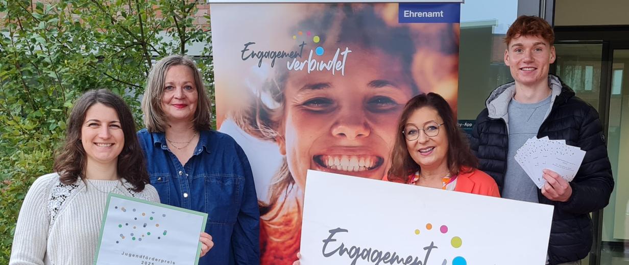 Vier Personen stehen neben einem Rollup-Poster.