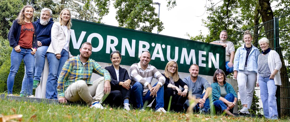 Betriebsbesichtigung Vornbäumen Eine Personengruppe steht, hockt und sitzt vor einem Zaun.
