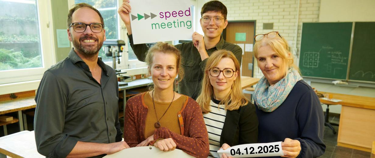 Fünf Personen stehen in einem Klassenraum.